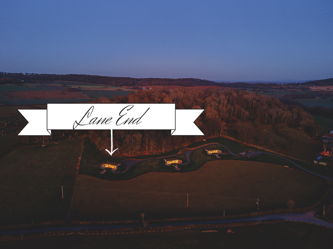 Aerial view of Lane End cabins at dusk, surrounded by countryside and highlighted with a banner.