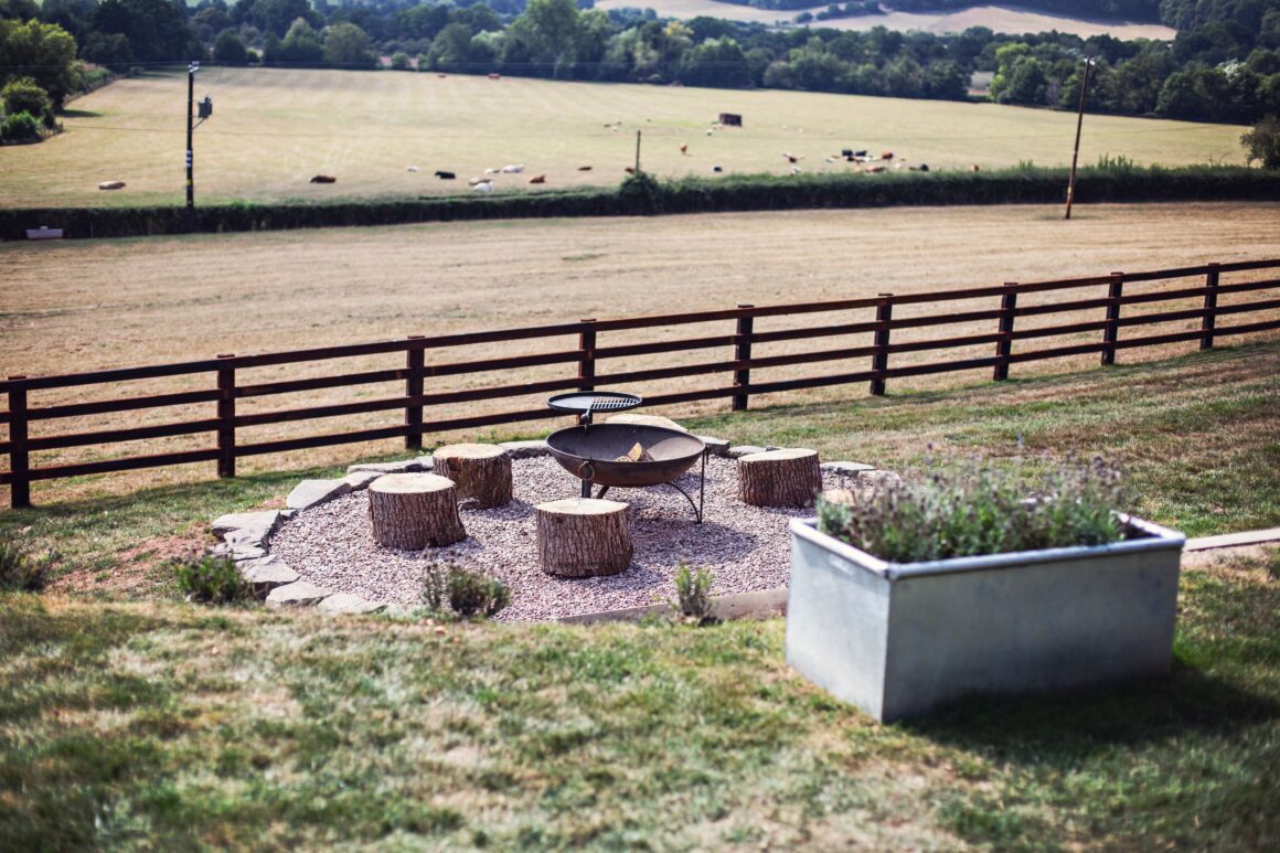Outdoor fire pit area with tree stump seating and countryside views.