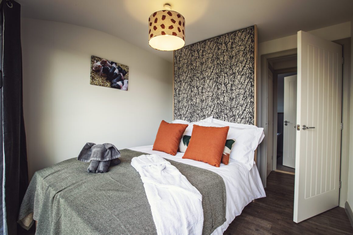 Cozy double bed in a modern cabin room with orange accent pillows and nature-themed decor.