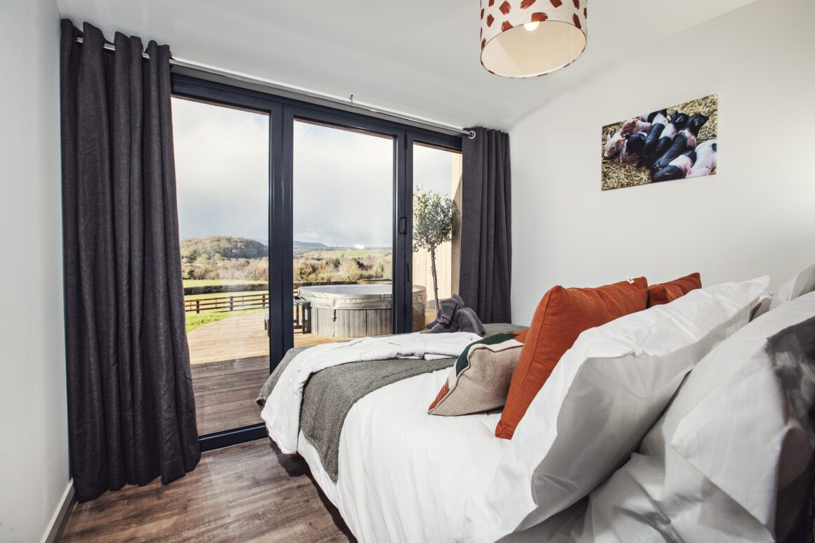 Cozy double bed in a modern cabin room with orange accent pillows and nature-themed decor.