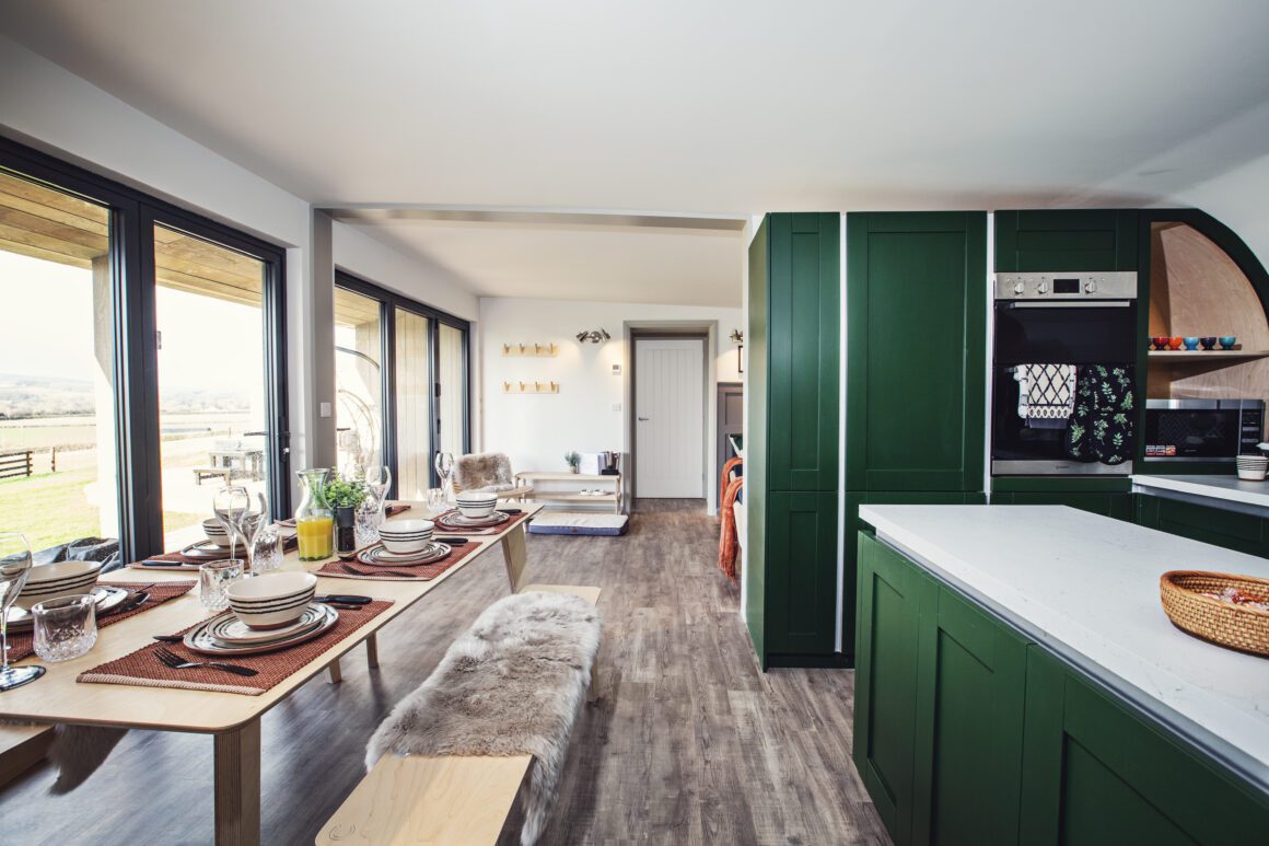 Spacious open-plan kitchen and dining area with green cabinets and a large table set for a meal.