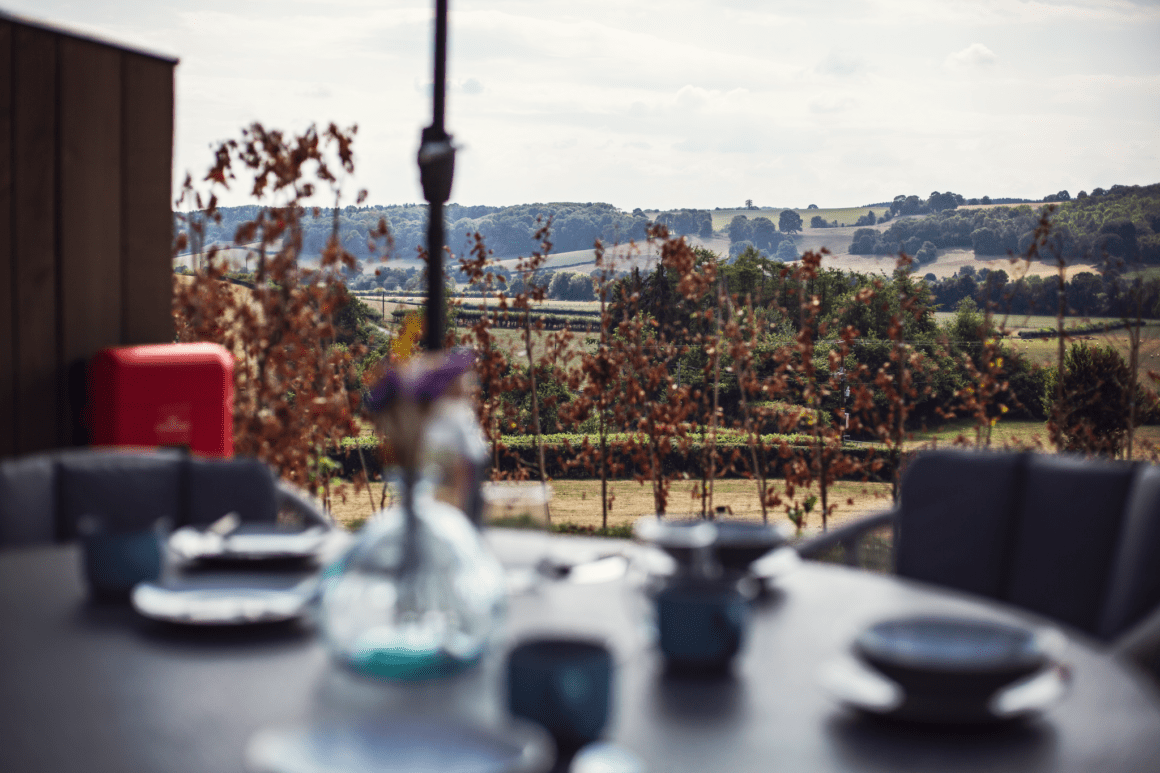 Scenic countryside view from an outdoor dining table set with plates and glassware.
