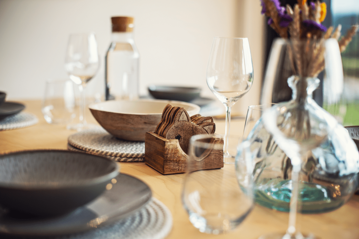 Elegant dining table setup with wine glasses, ceramic plates, and rustic wooden coasters.