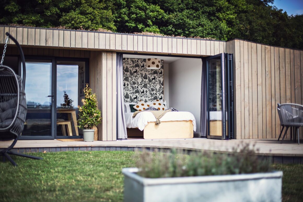 Modern cabin with open bedroom doors, nature-themed decor, and outdoor seating on a wooden deck