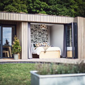 Modern cabin with open bedroom doors, nature-themed decor, and outdoor seating on a wooden deck