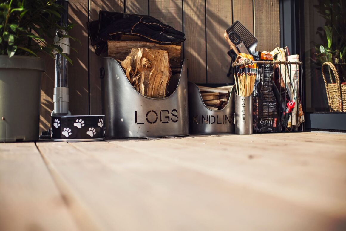Outdoor firewood setup with logs, kindling, matches, and fire accessories on a wooden deck.