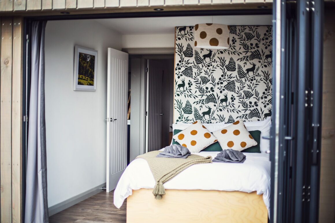 Cozy cabin bedroom with nature-themed accent wall, patterned pillows, and open doors.